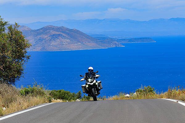 Ein Motorrad fährt durch ein Kurve in Griechenland vor blauem Meer