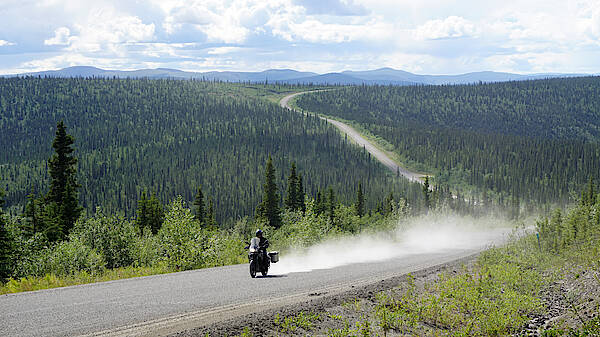 Ein Motorrad zieht eine Staubfahne auf dem Top of the World Highway in Alaska hinter sich her